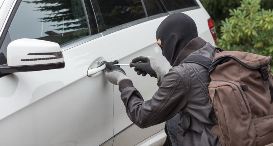 Thief breaking into a white automobile in a residential neighborhood